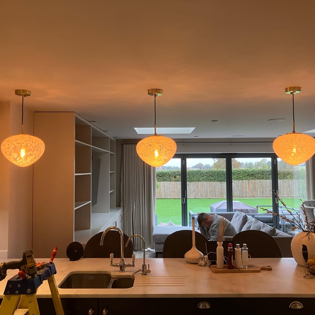 Three glass pendant lights fitted over a kitchen island with bi-fold doors to the garden